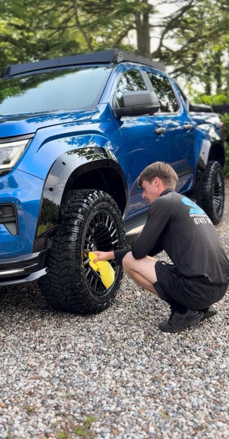 ST Valets detailer cleaning the alloy wheels on a blue lifted pickup truck